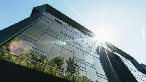 Low angle view of a modern skyscraper with reflections and sun flare, emphasizing contemporary architecture.